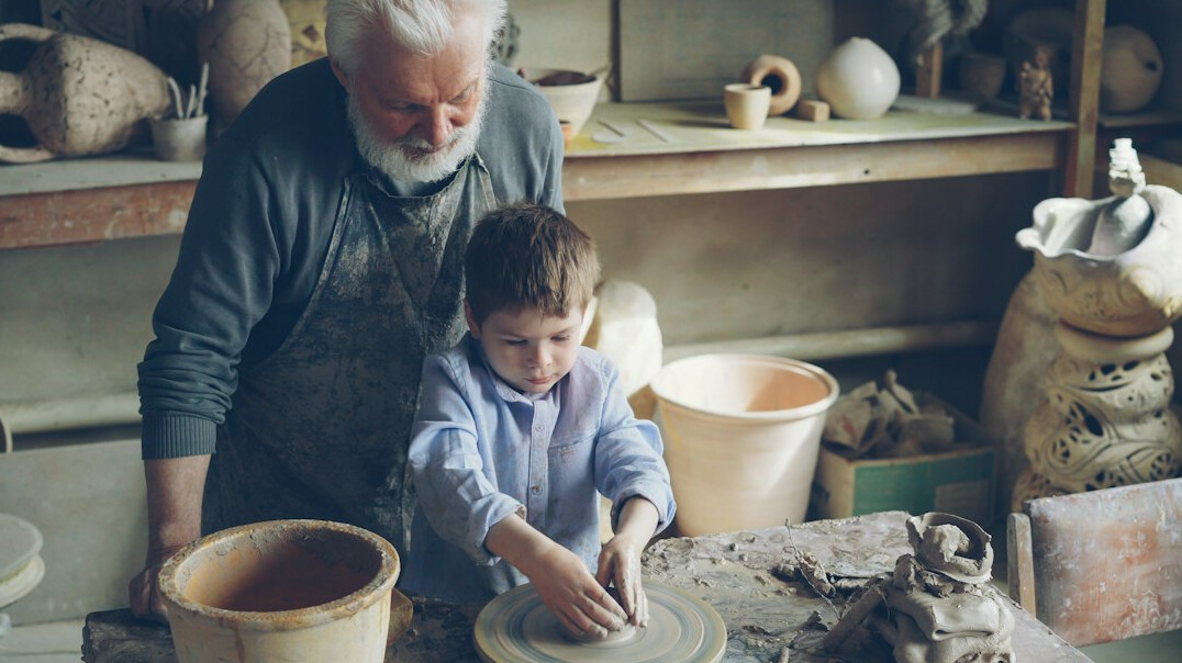 elderly artisan teaching young apprentice